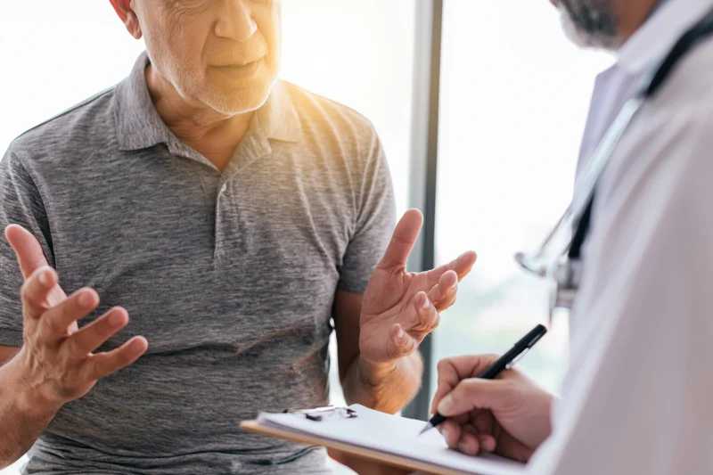 Elderly man gesturing while talking to doctor during medical consultation in clinic