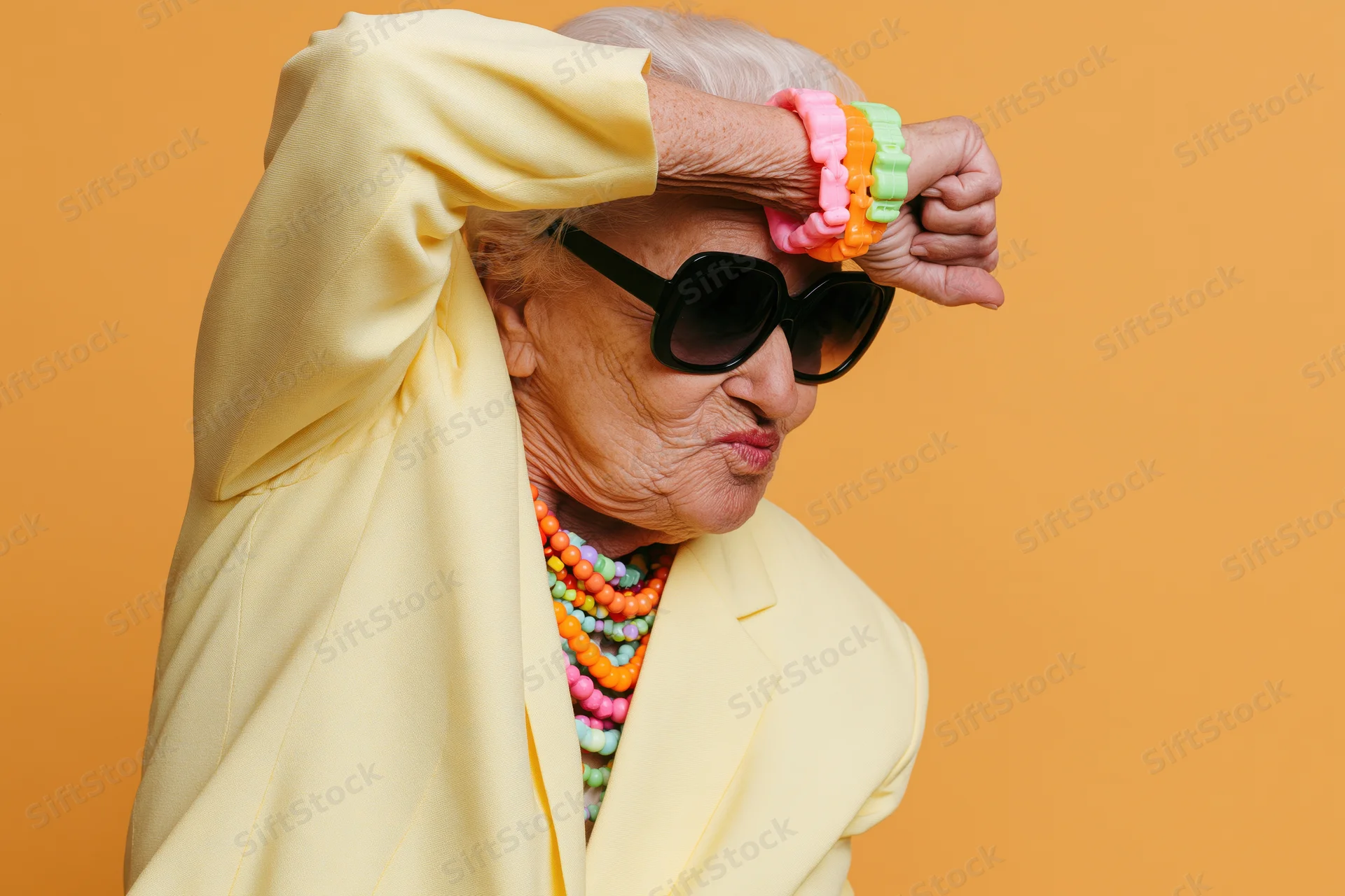 Elderly woman in yellow blazer doing dab pose with sunglasses and colorful jewelry against orange background