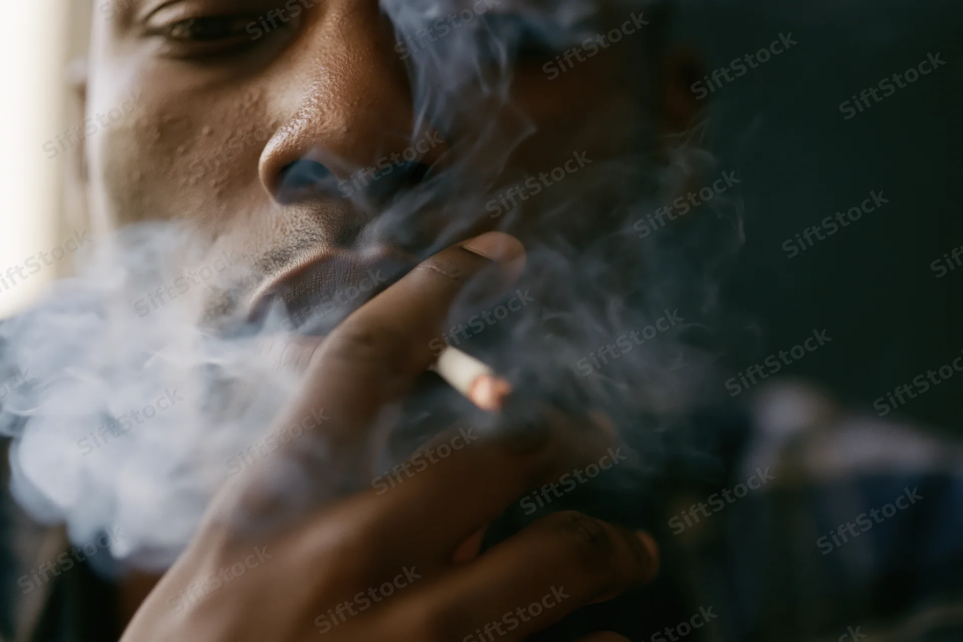 Young black man smoking a cigarette, exhaling smoke, close-up of lower face and hand