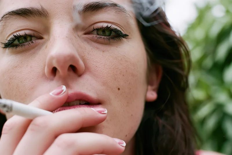 Young woman smoking a cigarette outdoors, close-up on her face and green eyes