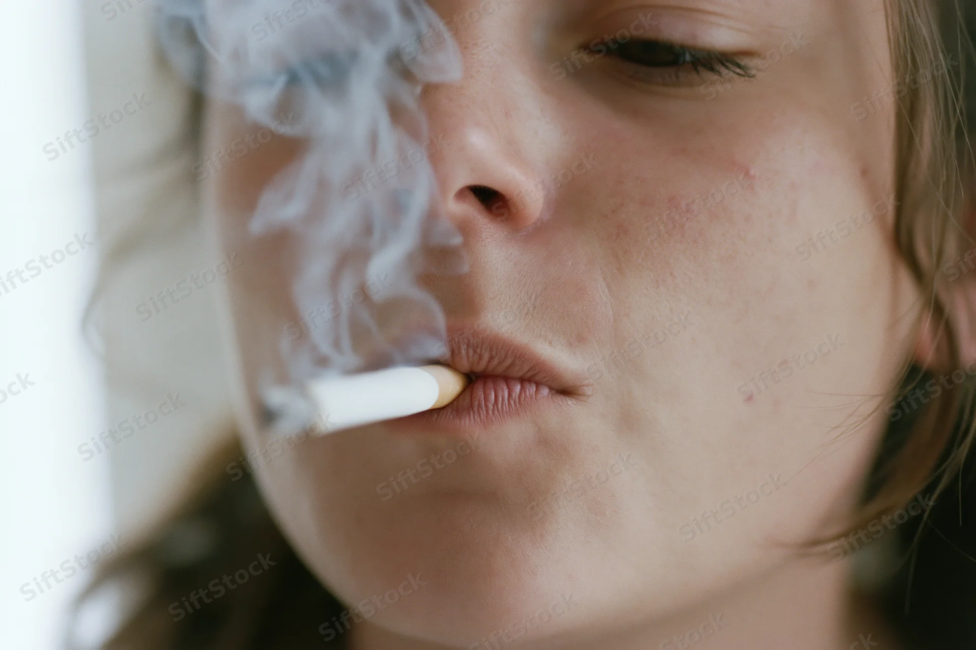 Young woman smoking a cigarette in close-up view with smoke rising from her lips
