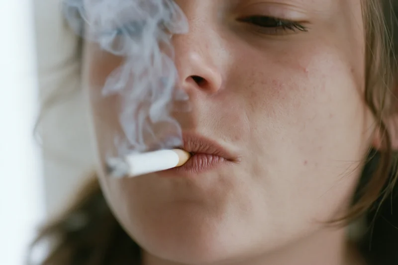 Young woman smoking a cigarette in close-up view with smoke rising from her lips