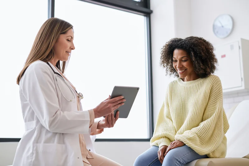 Female doctor showing tablet to smiling patient during consultation in clinic