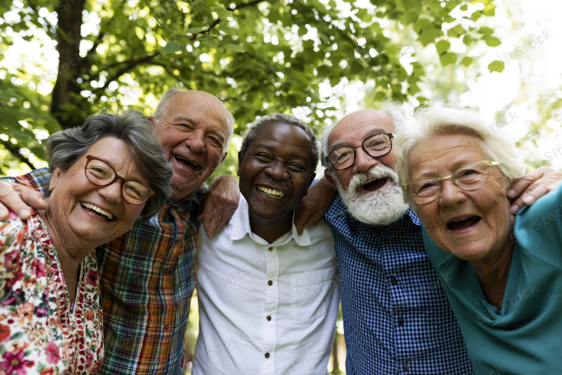 Five diverse senior friends smiling closely together outdoors under leafy trees