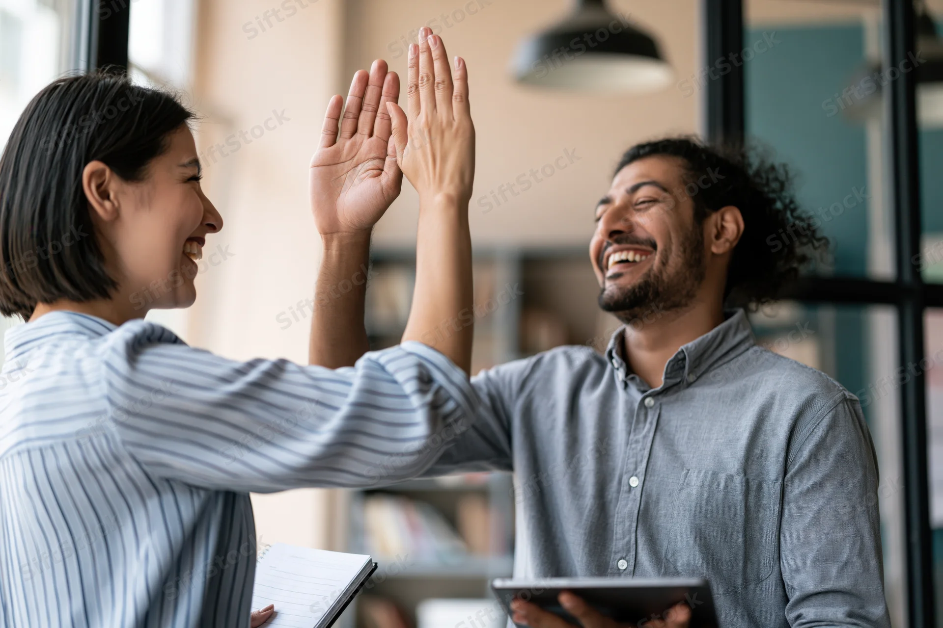 Woman and man colleagues high-fiving in modern office space