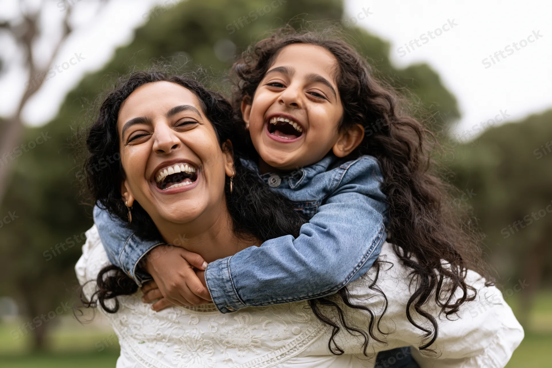Woman giving young daughter a piggyback ride in a park, both laughing joyfully