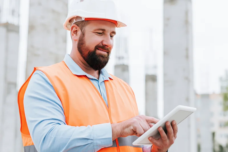 Male construction engineer reviewing plans on tablet at building site