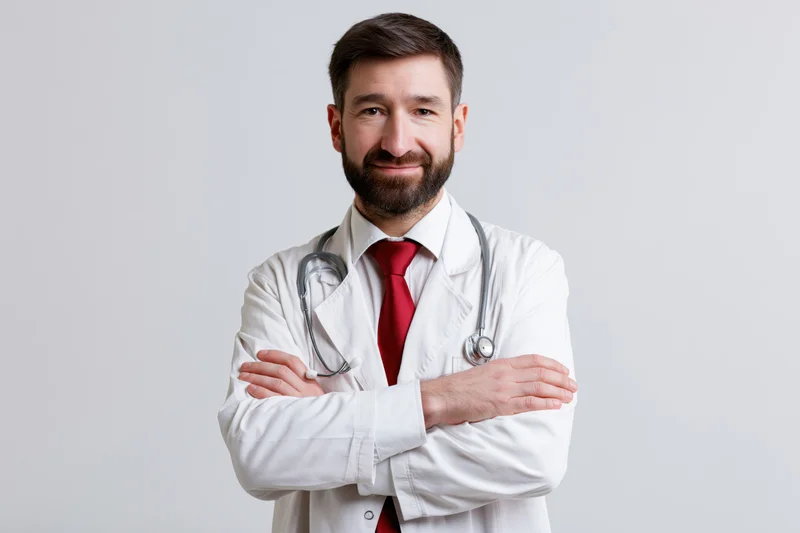 Male doctor with arms crossed wearing white coat and stethoscope in studio setting