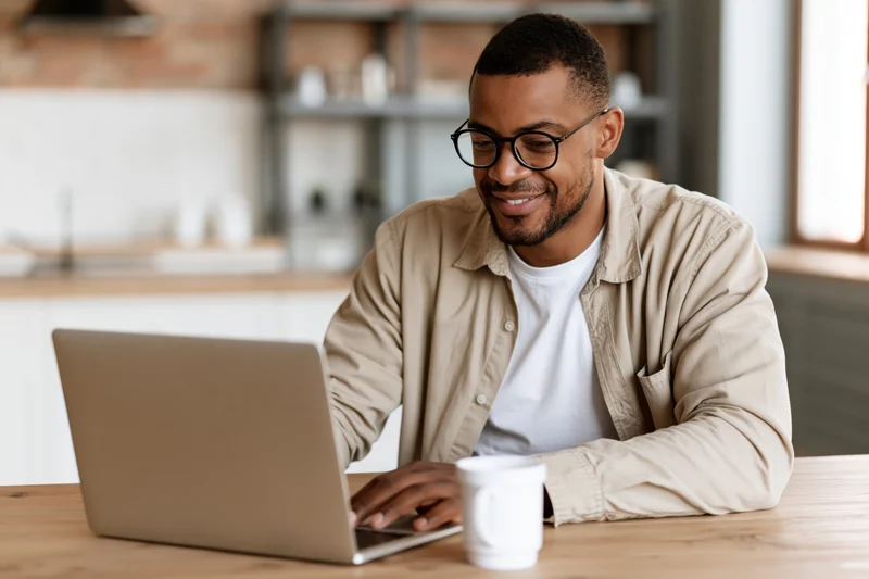 Man working on laptop at wooden dining table in home office setting