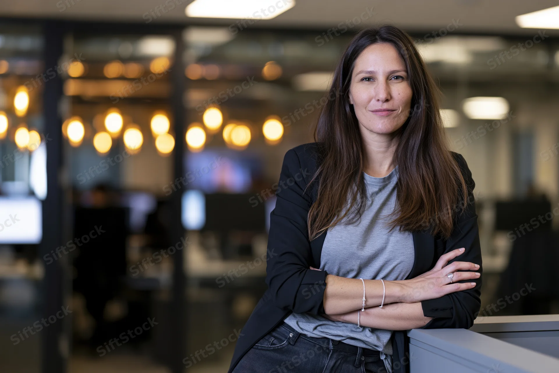 Woman with arms crossed leaning against desk in modern office interior