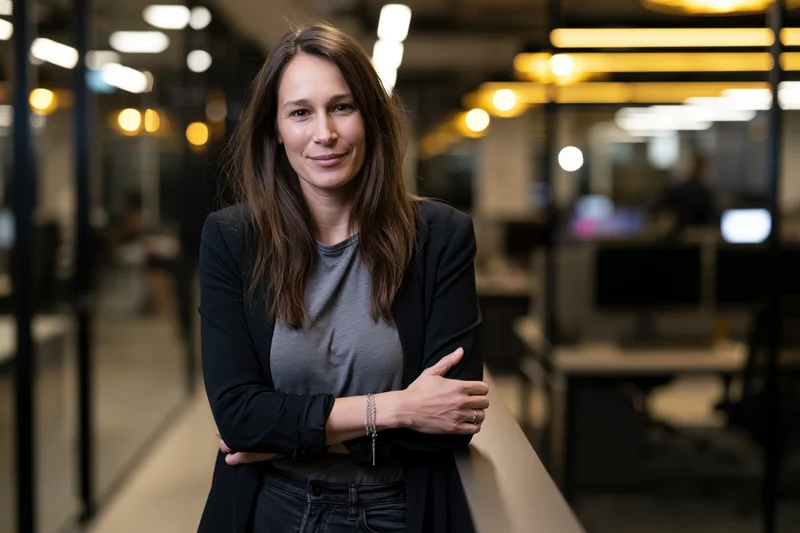 Woman leaning against railing in modern office space with arms crossed and smiling