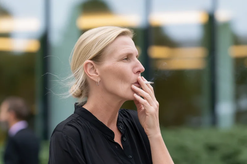 Middle-aged blonde woman smoking a cigarette outdoors near an office building