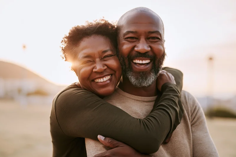 Middle-aged african american couple embracing and laughing outdoors in a sunlit field