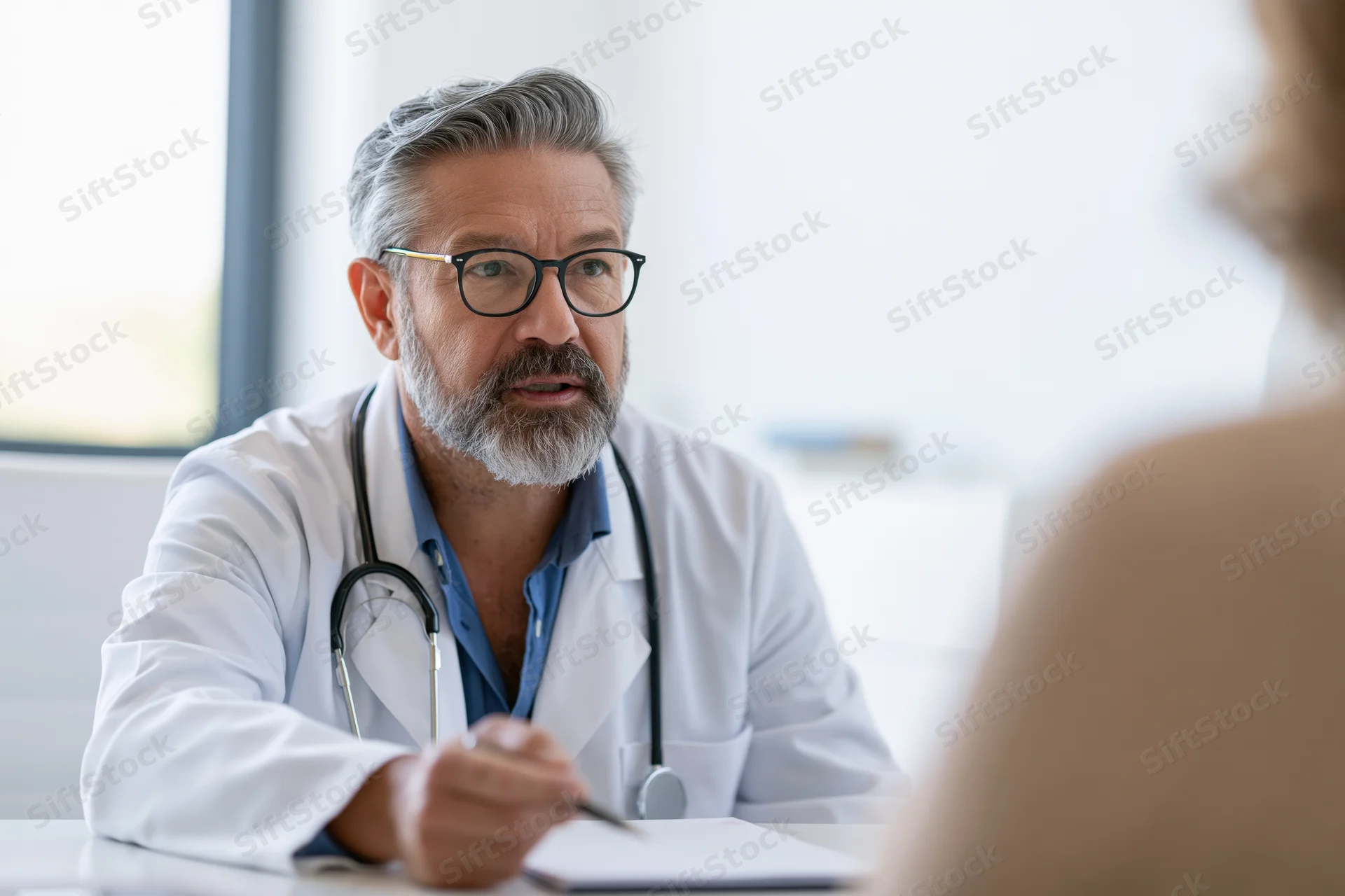 Male doctor in lab coat with stethoscope writing notes during patient consultation in clinic office