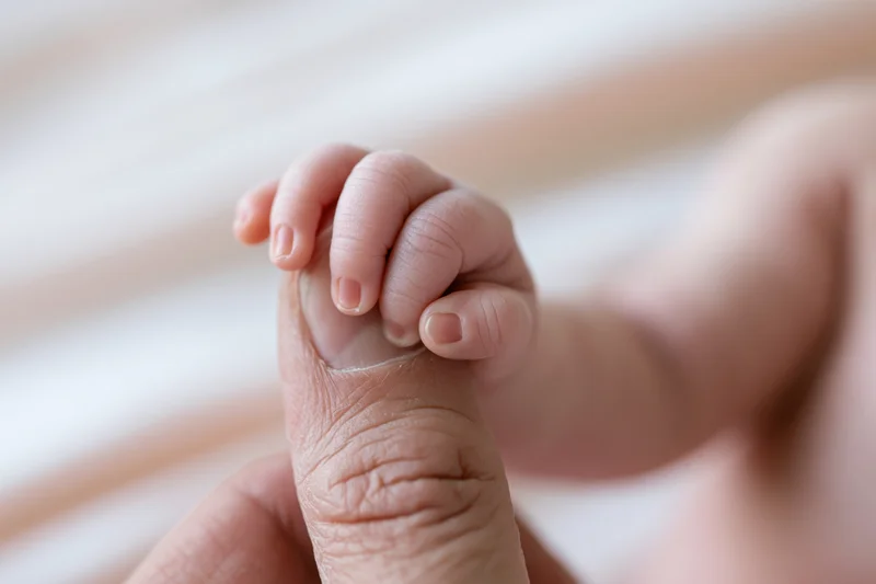 Newborn baby's tiny hand gripping an adult finger close-up