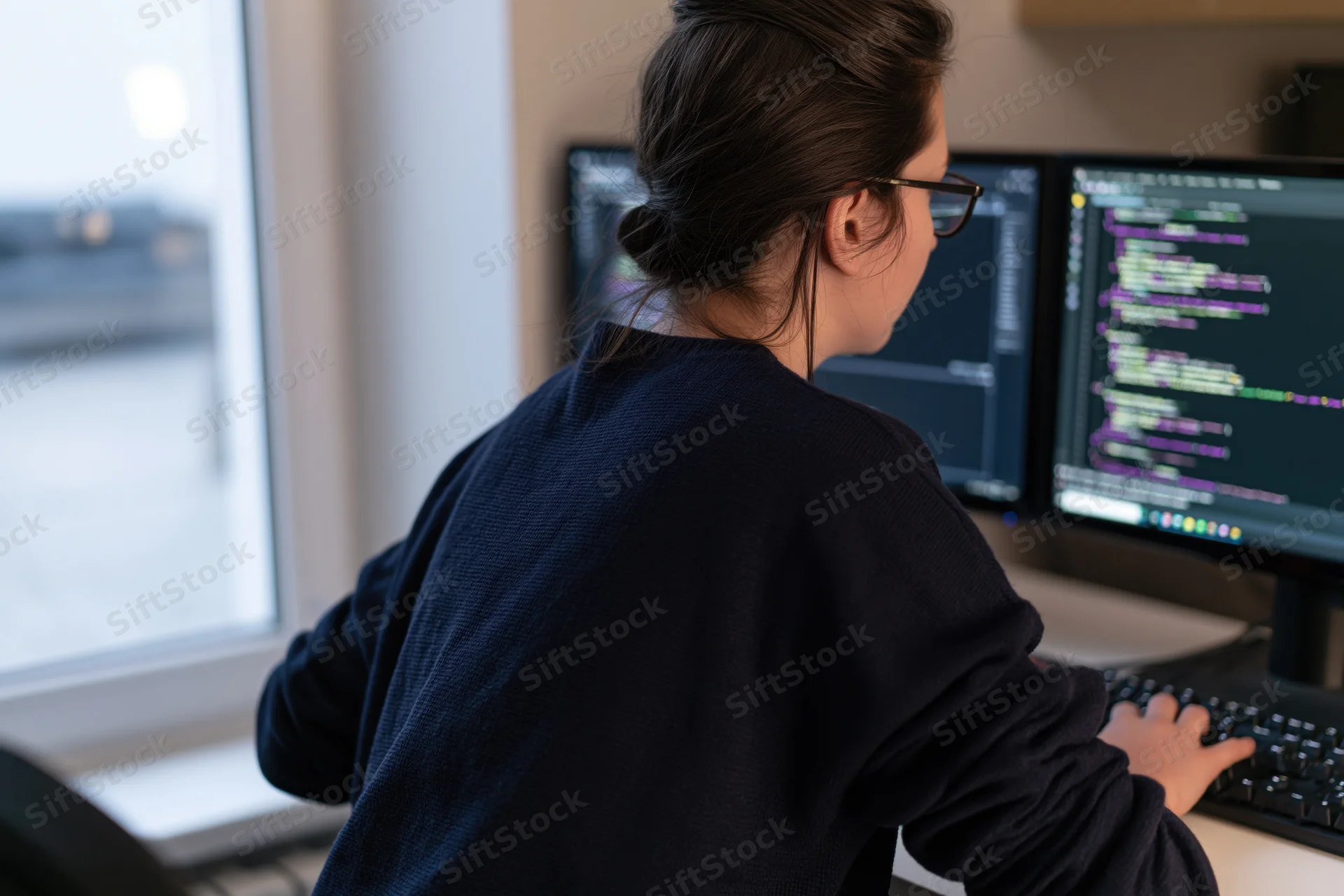 Young woman software developer coding at dual monitors in office workspace
