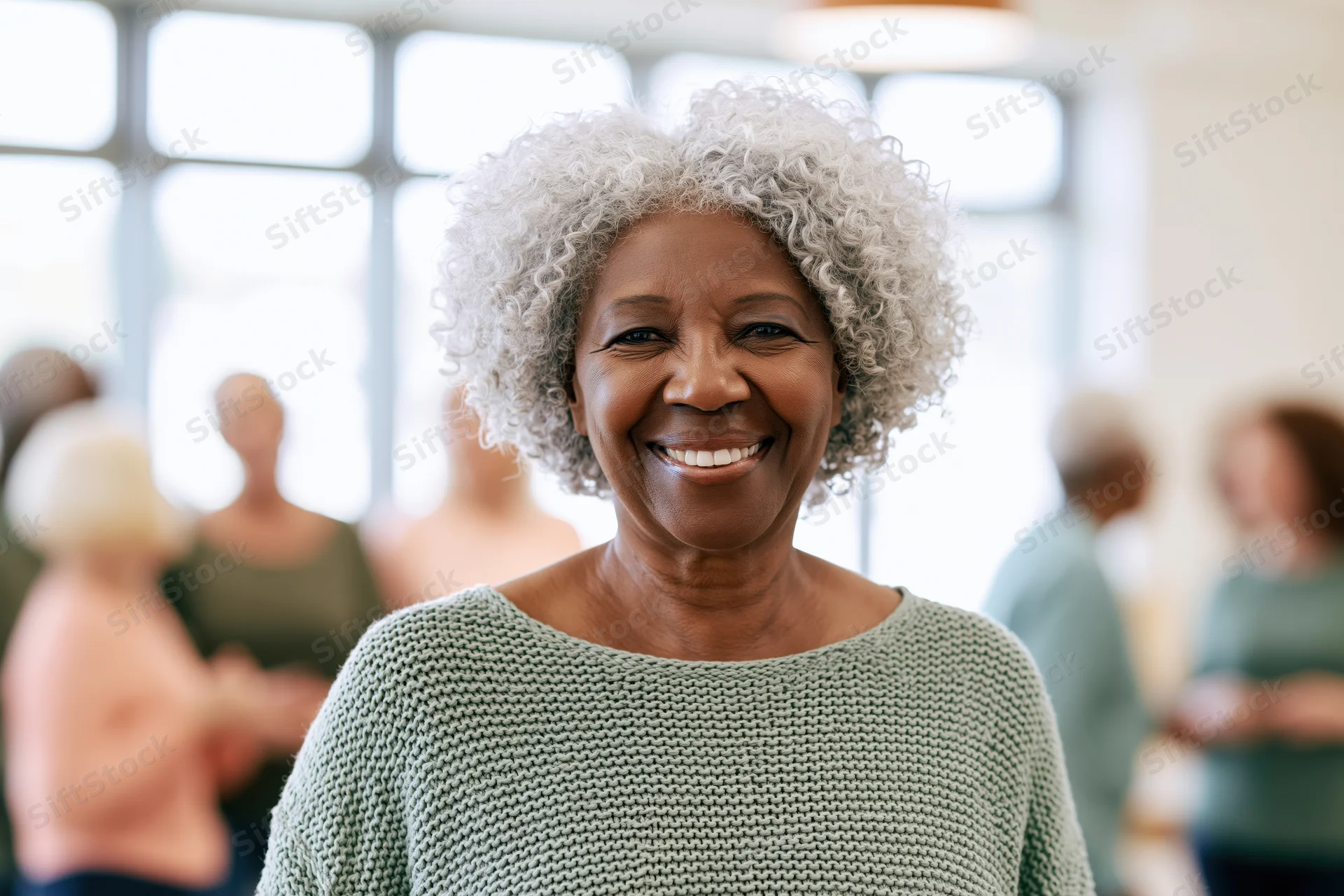 Senior black woman smiling in a knit sweater with curly silver-grey hair in a group setting indoors