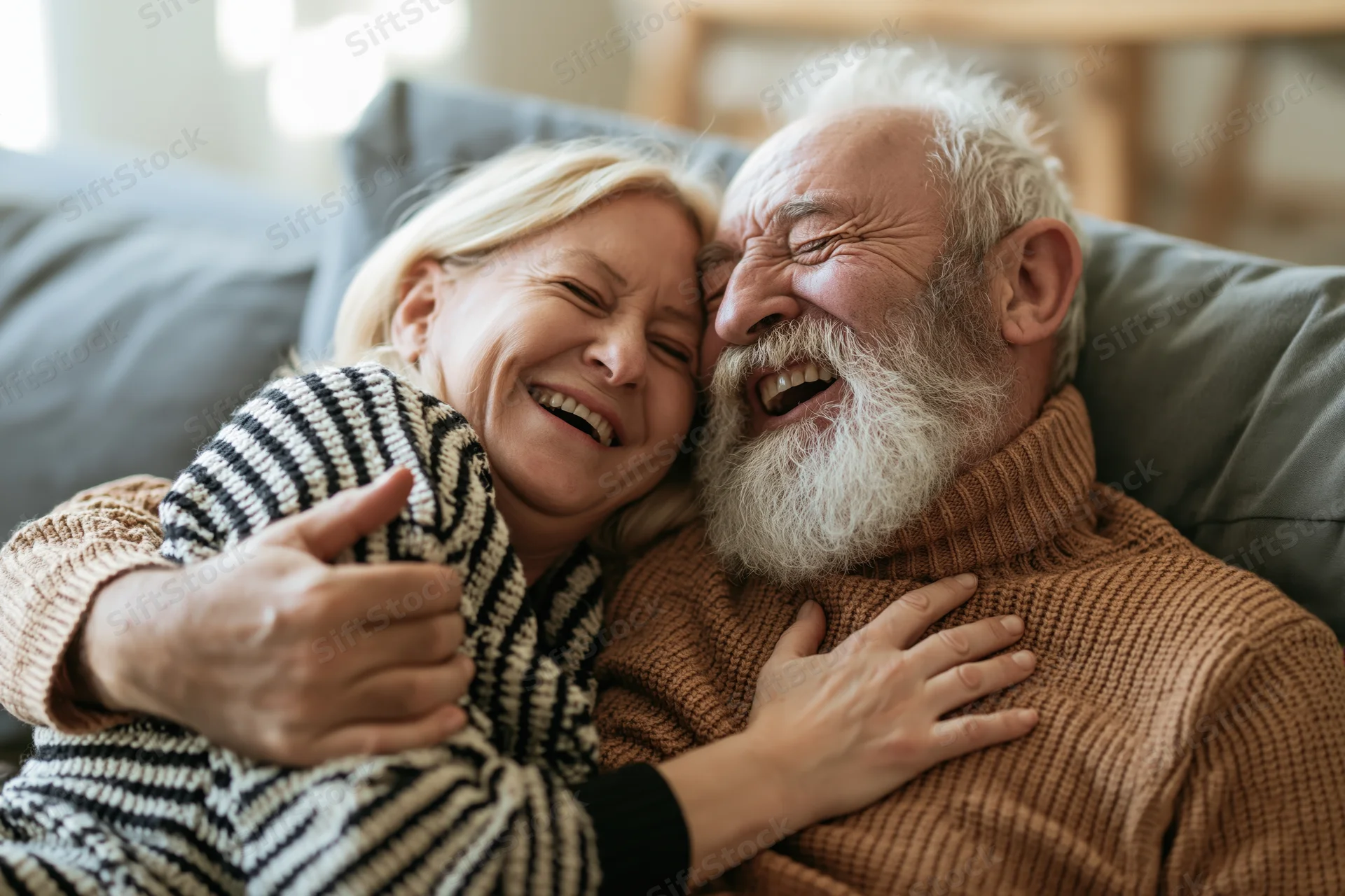 Senior couple laughing and embracing on a grey sofa in a cozy living room