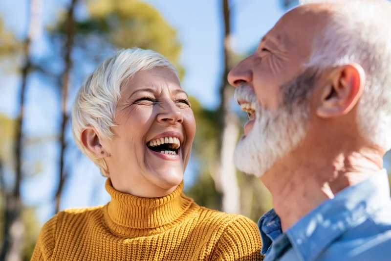 Senior couple laughing together outdoors in a sunny park