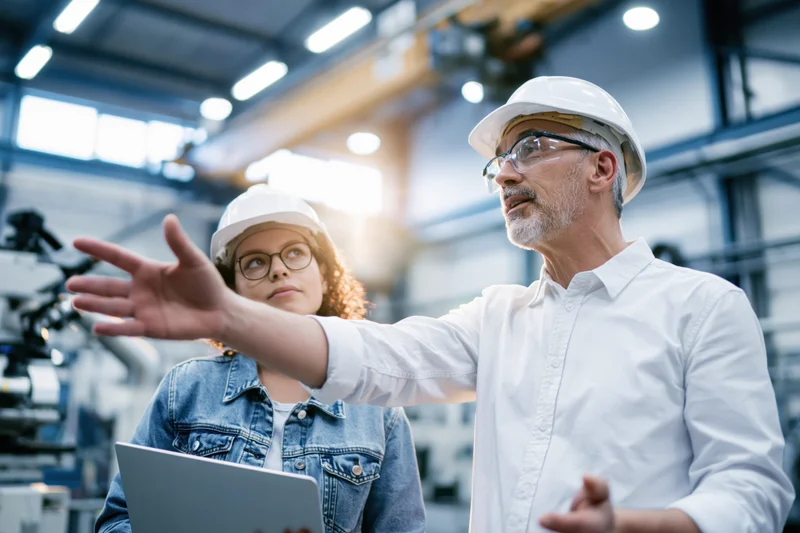 Senior male engineer gesturing while discussing with young woman in factory workshop