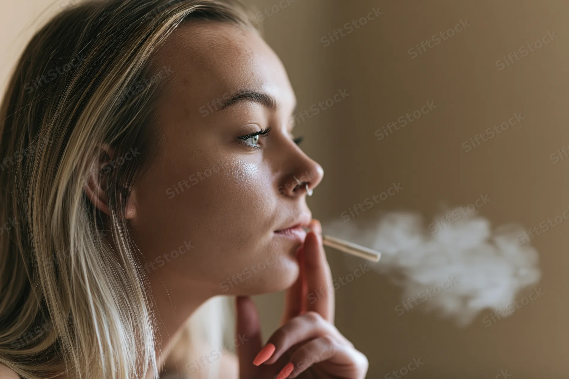 Young blonde woman exhaling cigarette smoke in profile indoors