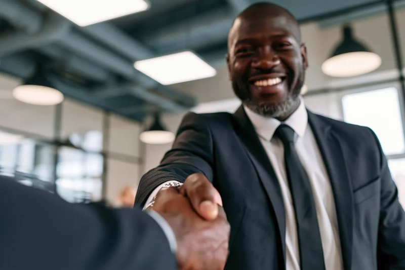 Smiling black businessman in dark suit shaking hands in modern office