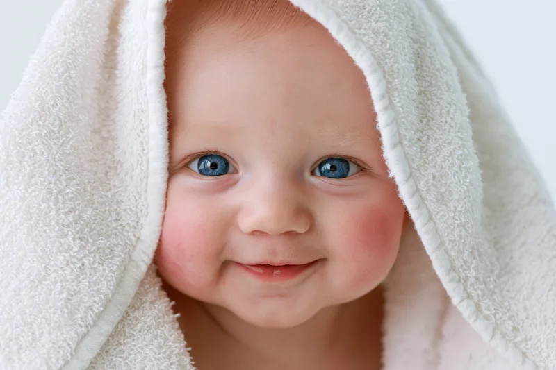 Smiling baby with bright blue eyes peeking from under a hooded towel