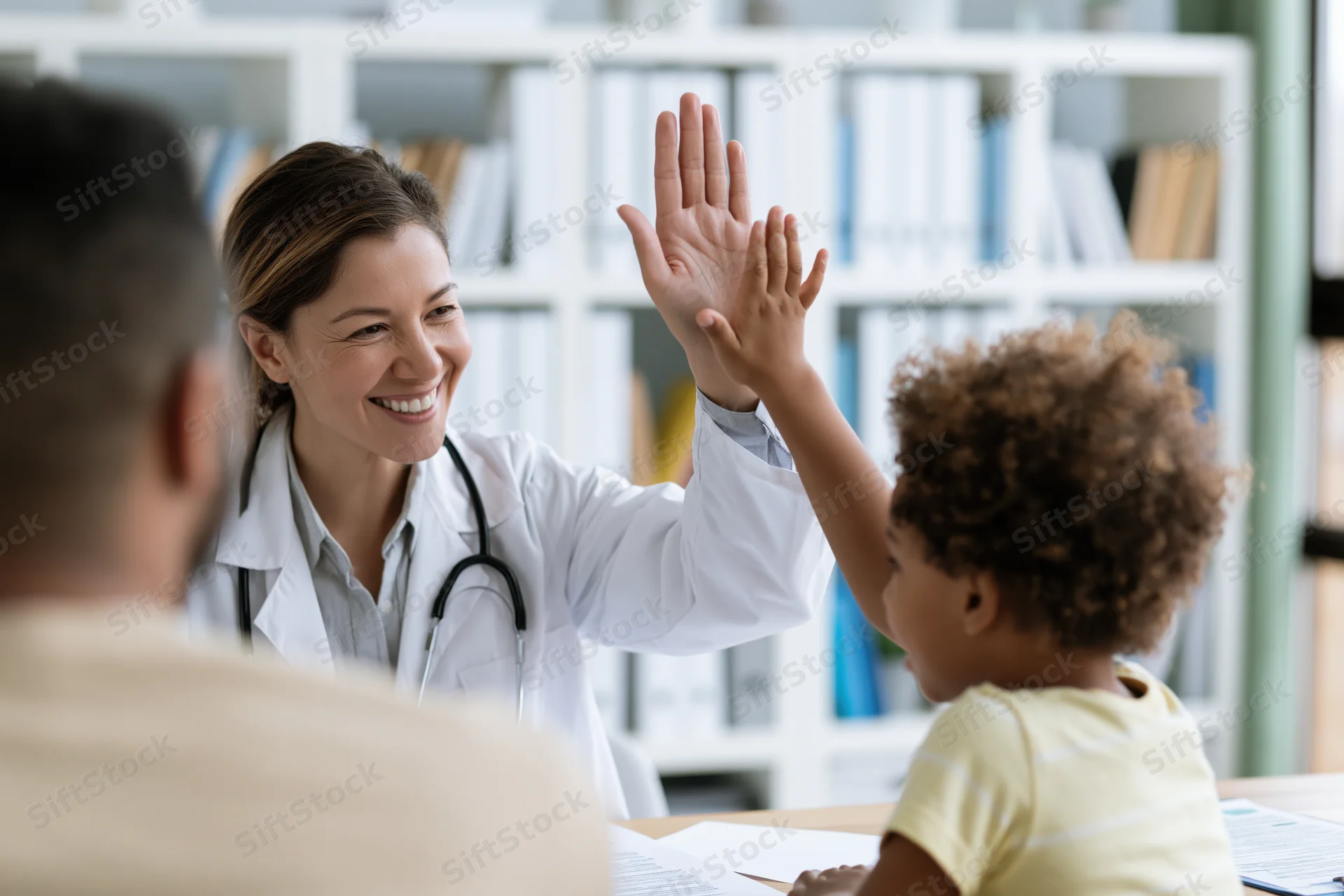 Female doctor giving high-five to young child during clinic visit with parent present