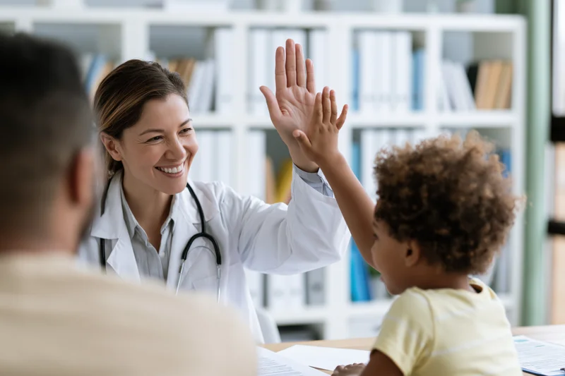 Female doctor giving high-five to young child during clinic visit with parent present