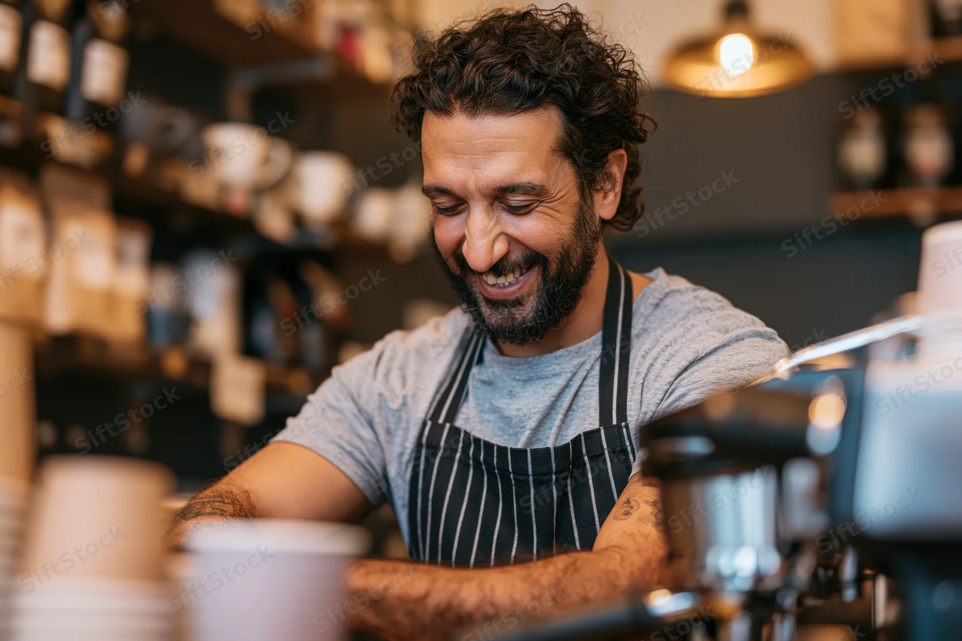 Smiling male barista with curly dark hair and beard operating coffee machine in cafe