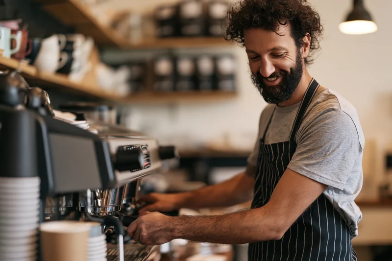 Smiling male barista operating espresso machine in a cafe