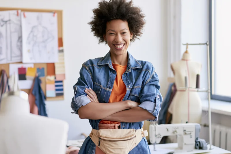 Smiling young black woman with arms crossed in fashion design studio