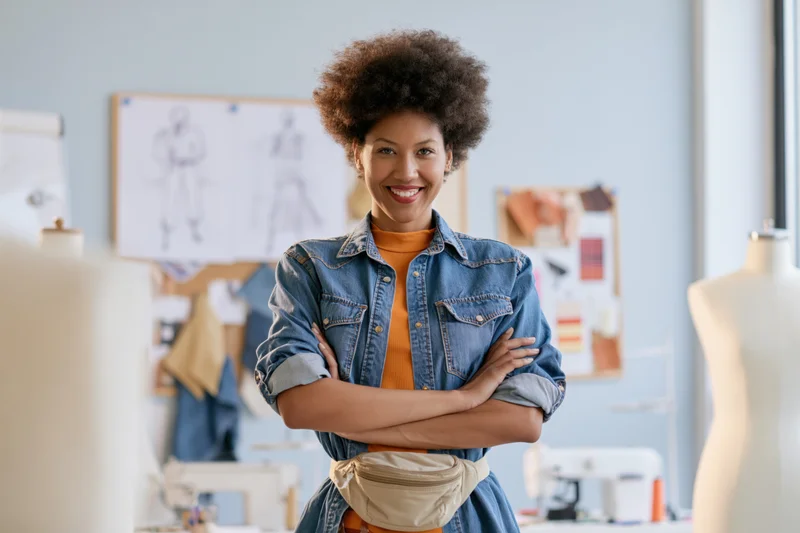 Smiling young black woman with arms crossed in fashion design studio