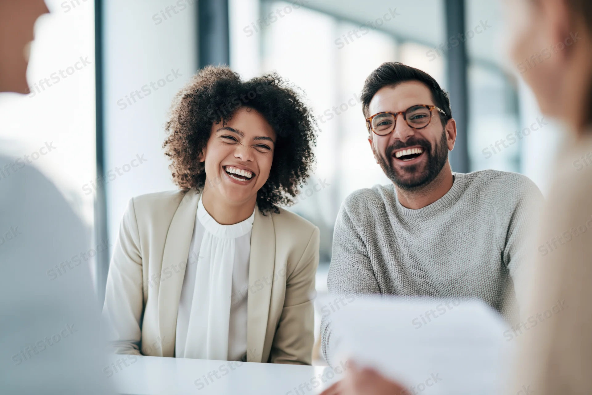 Coworkers laughing together during a casual meeting in a modern office