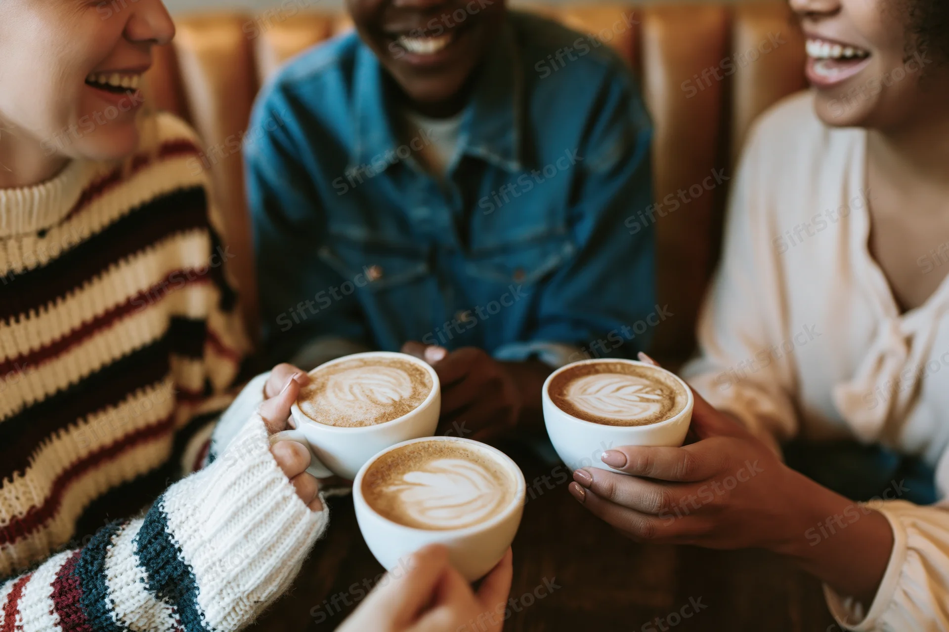 Three women laughing together at a cafe table holding cappuccinos