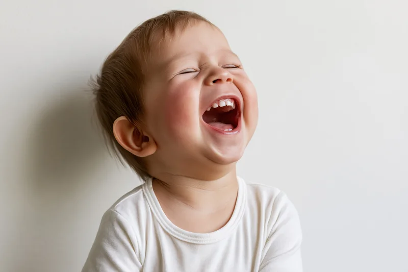 Toddler laughing with mouth wide open and eyes squinted shut against a plain white background