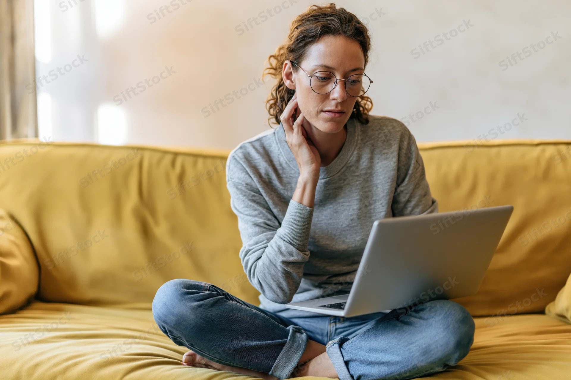 Woman sitting cross-legged on yellow sofa using laptop at home
