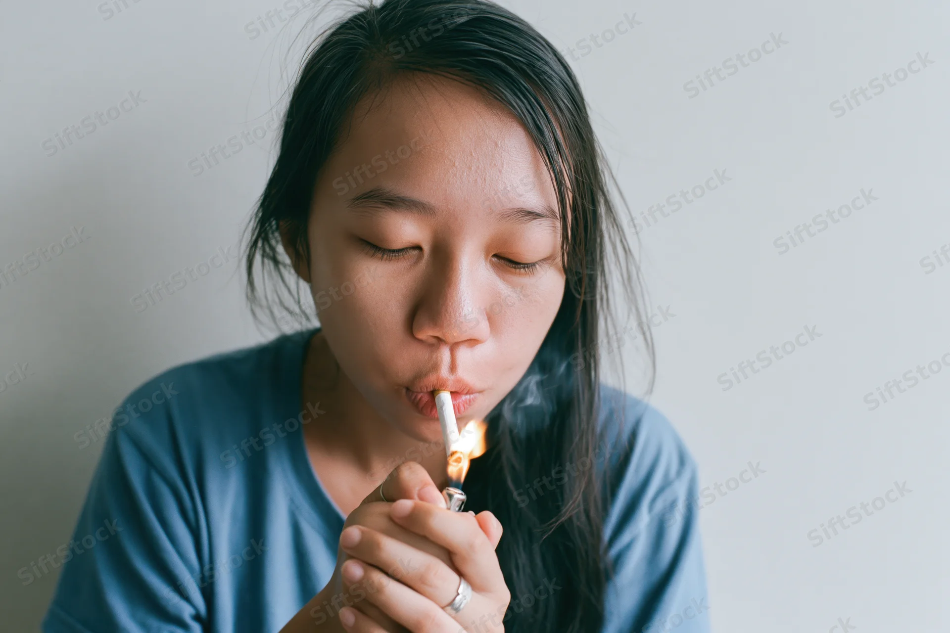 Young asian woman lighting a cigarette held between her lips indoors