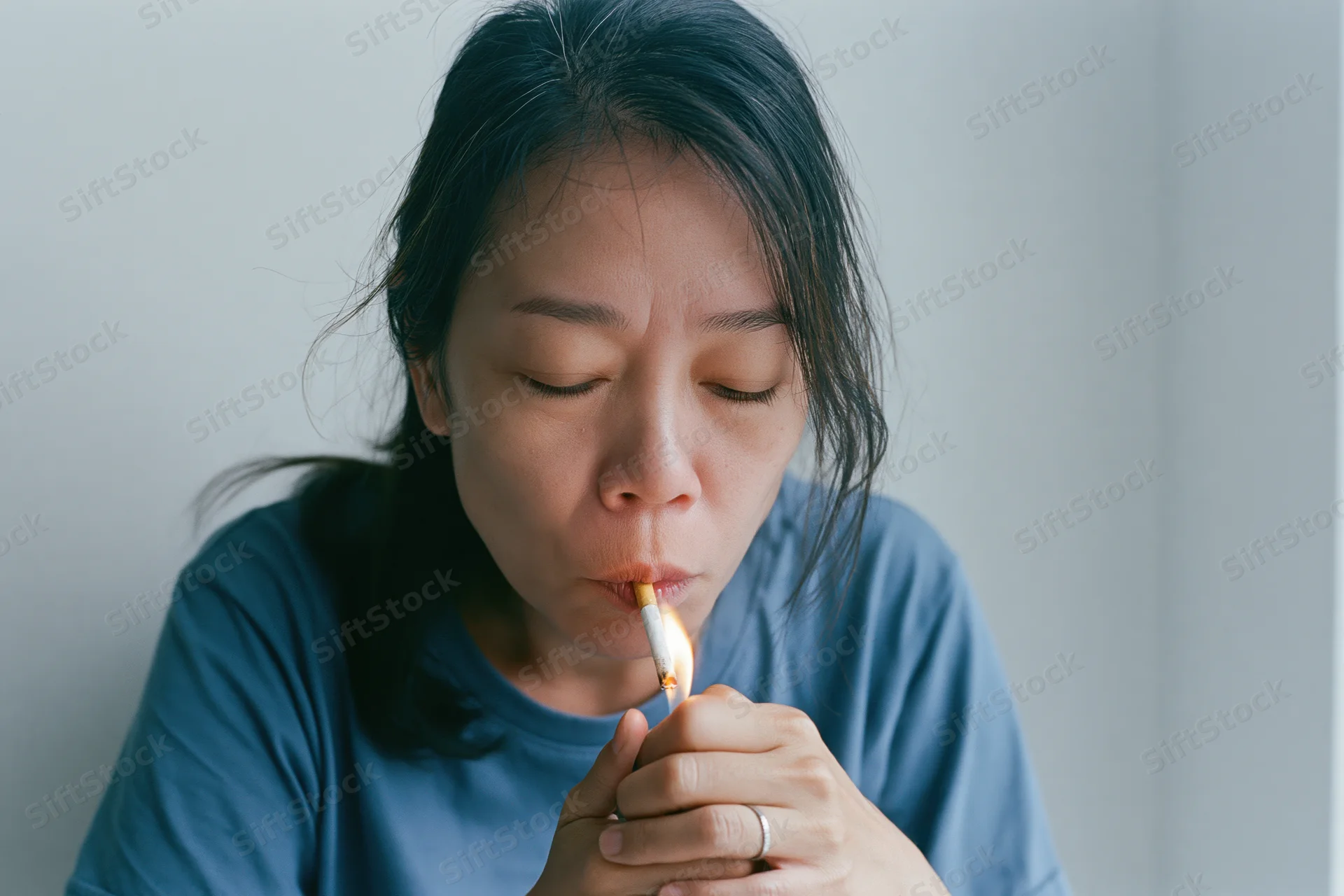 Asian woman lighting a cigarette held between her lips indoors