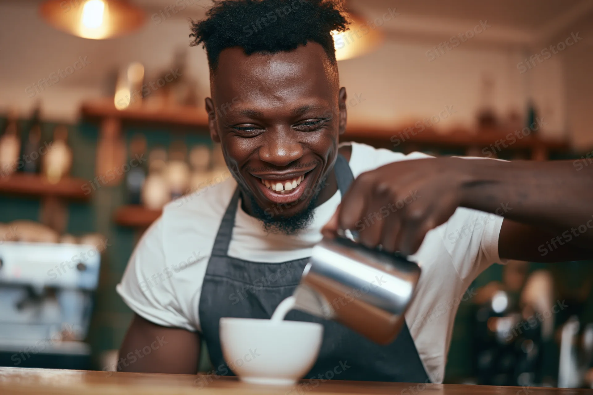 Young black male barista smiling while pouring steamed milk into a white cup at a coffee shop counter