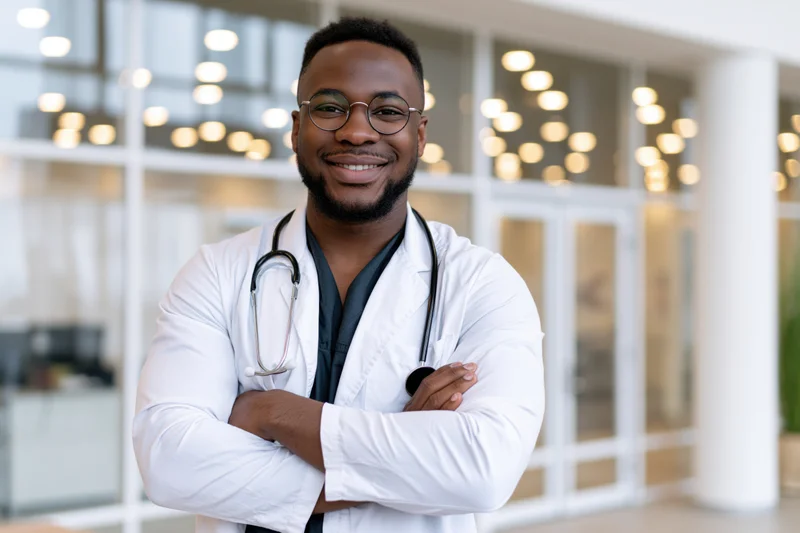 Black male doctor smiling with arms crossed in hospital corridor