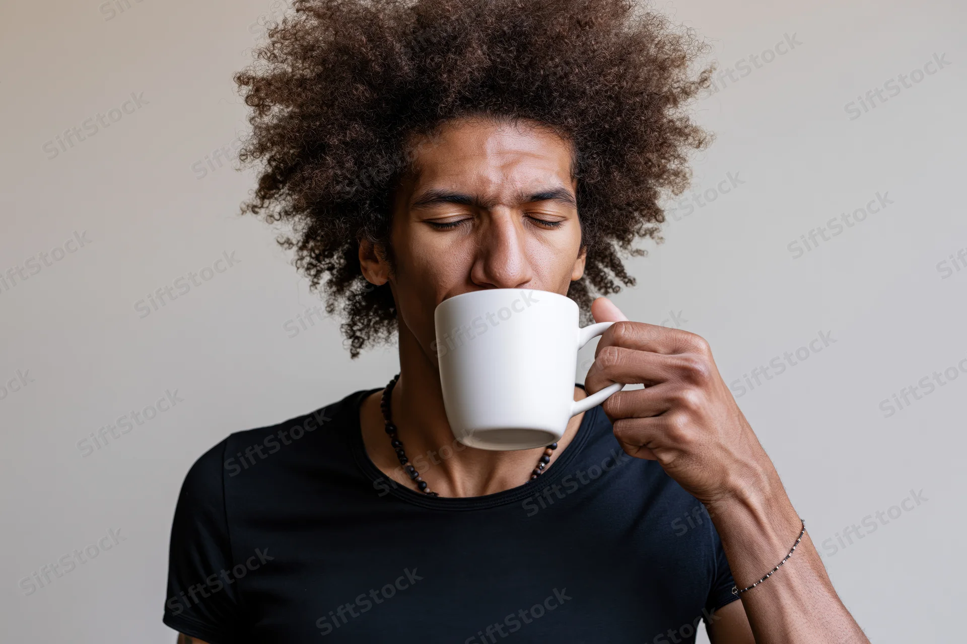 Young black man with afro drinking from a white mug indoors