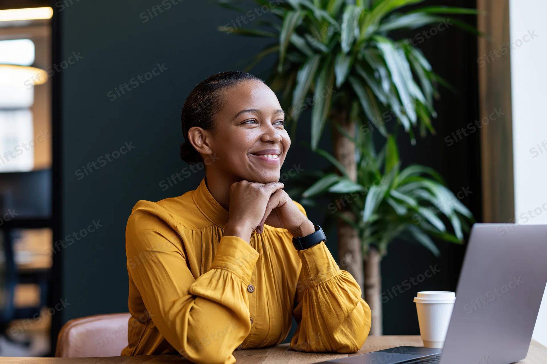 Young black woman smiling with hands clasped at desk in modern office
