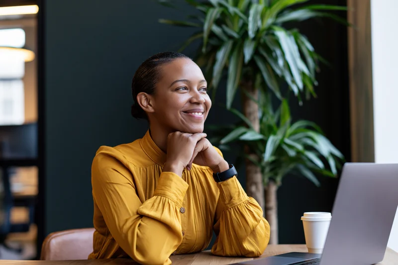 Young black woman smiling with hands clasped at desk in modern office