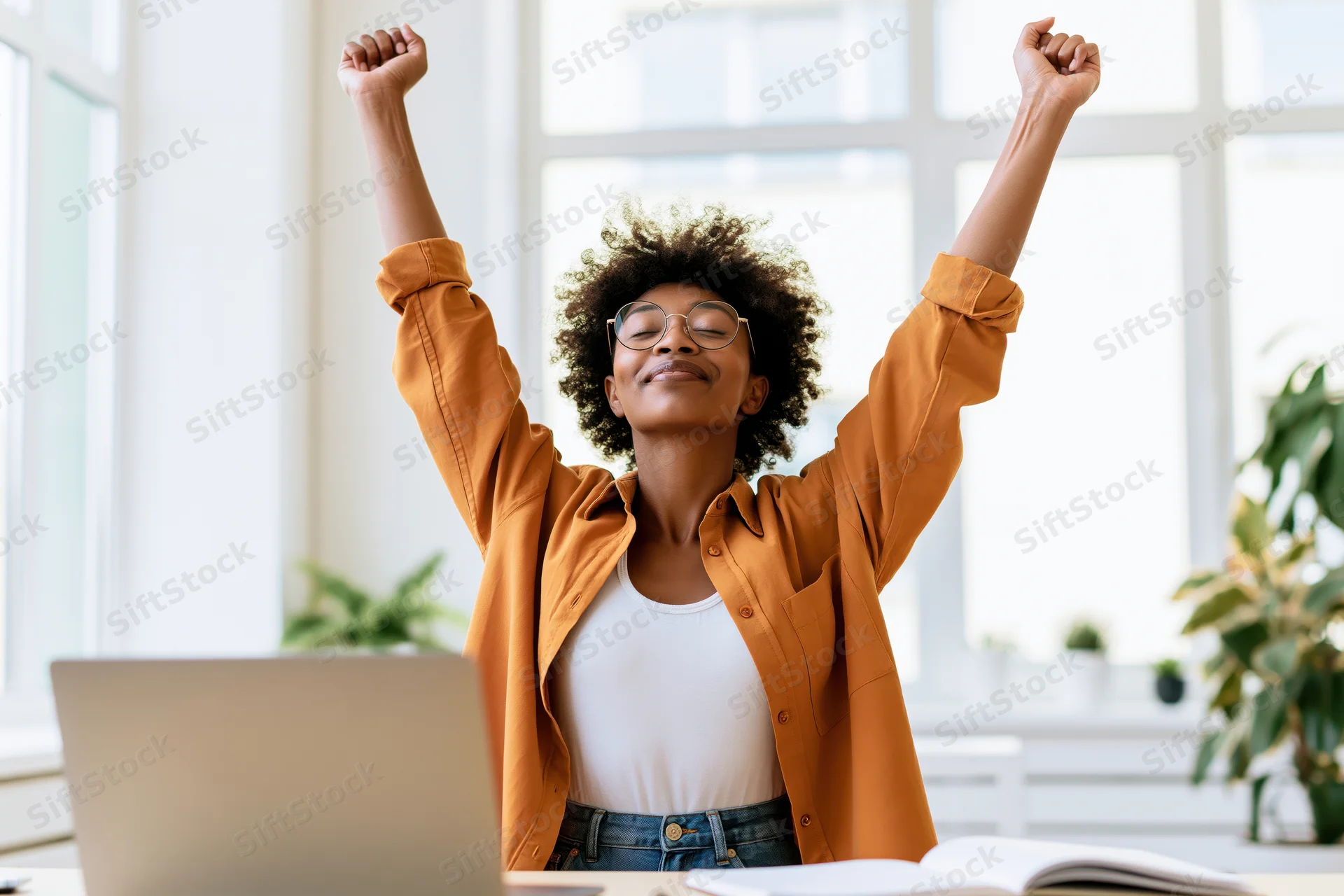 Young black woman celebrating with arms raised at office desk