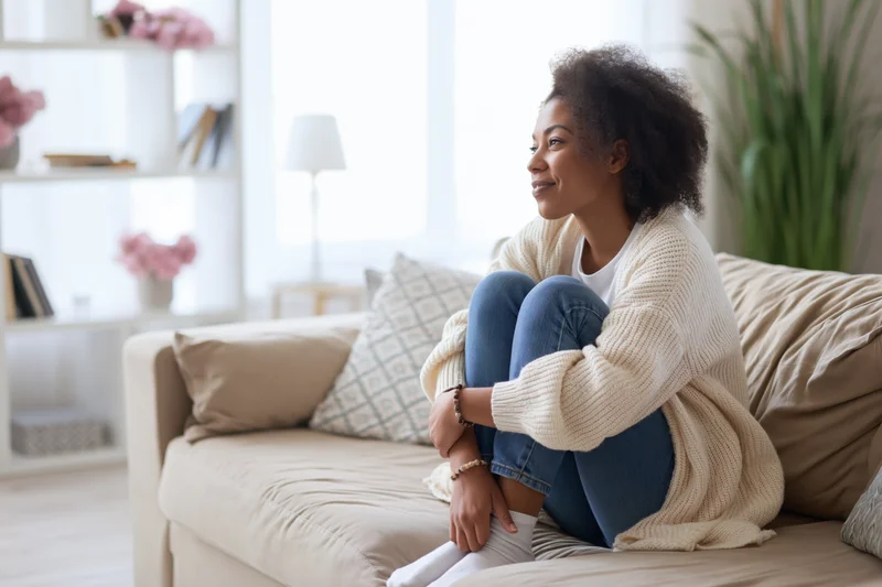 Young black woman sitting relaxed on beige sofa in bright living room