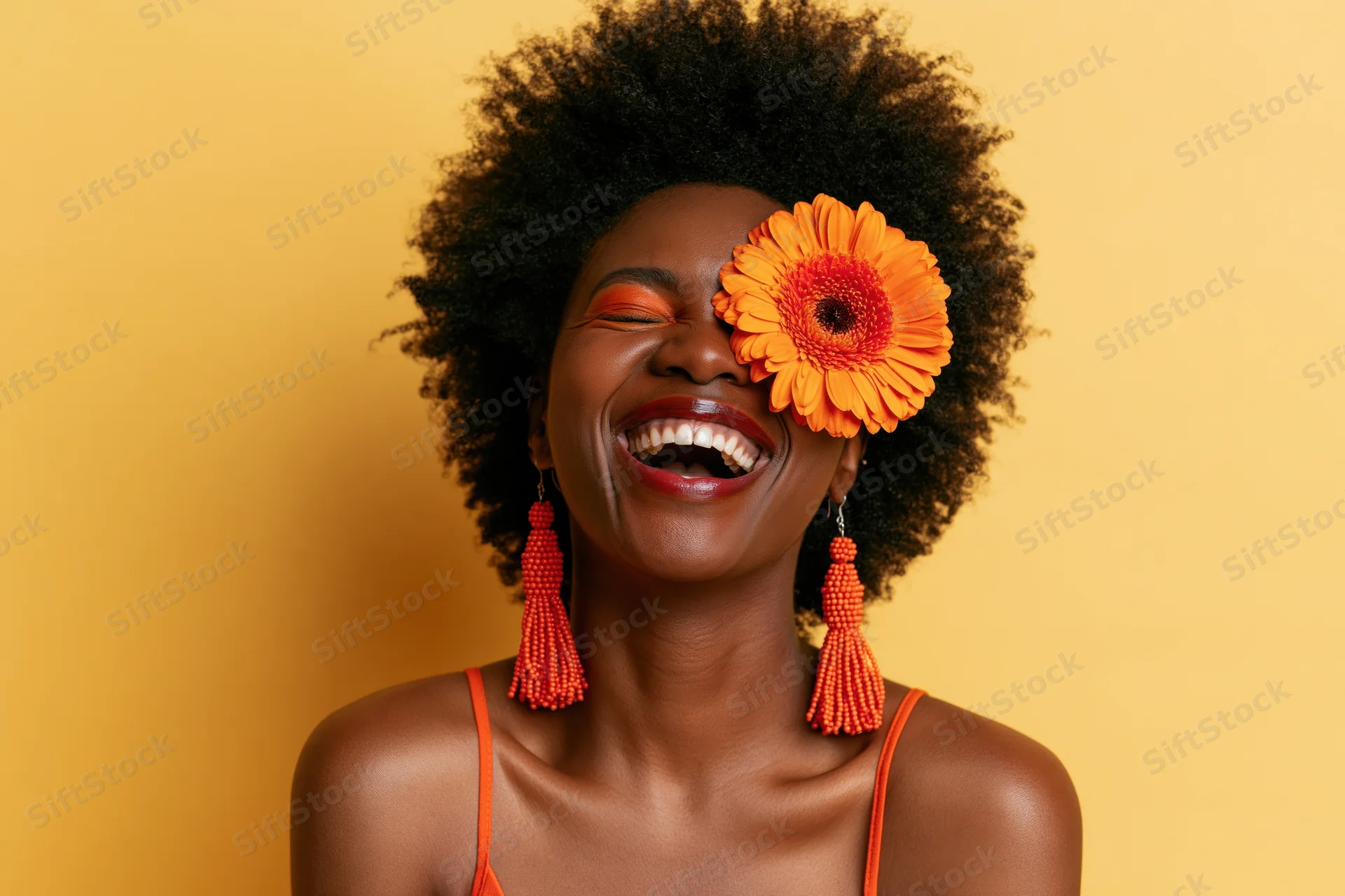 Black woman laughing with orange flower over eye against yellow background