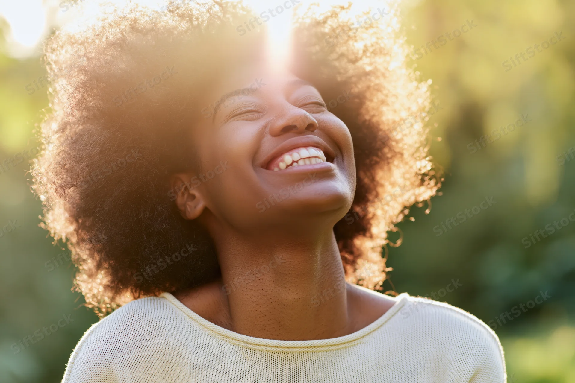 Young black woman laughing with head tilted back in sunlight outdoors