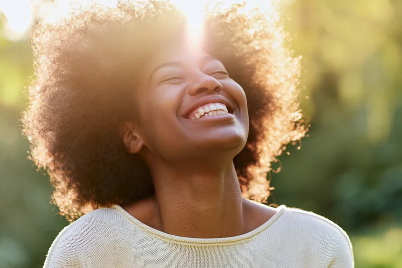 Young black woman laughing with head tilted back in sunlight outdoors