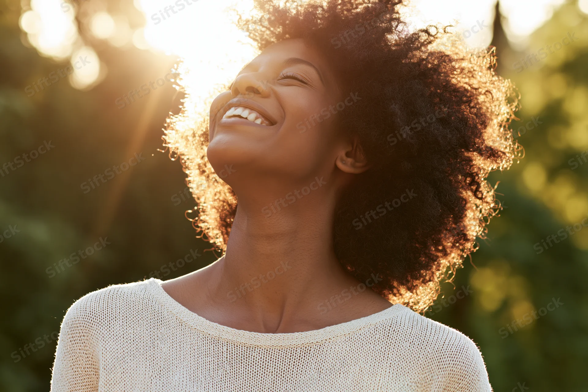 Young black woman laughing with head tilted back in sunlight outdoors